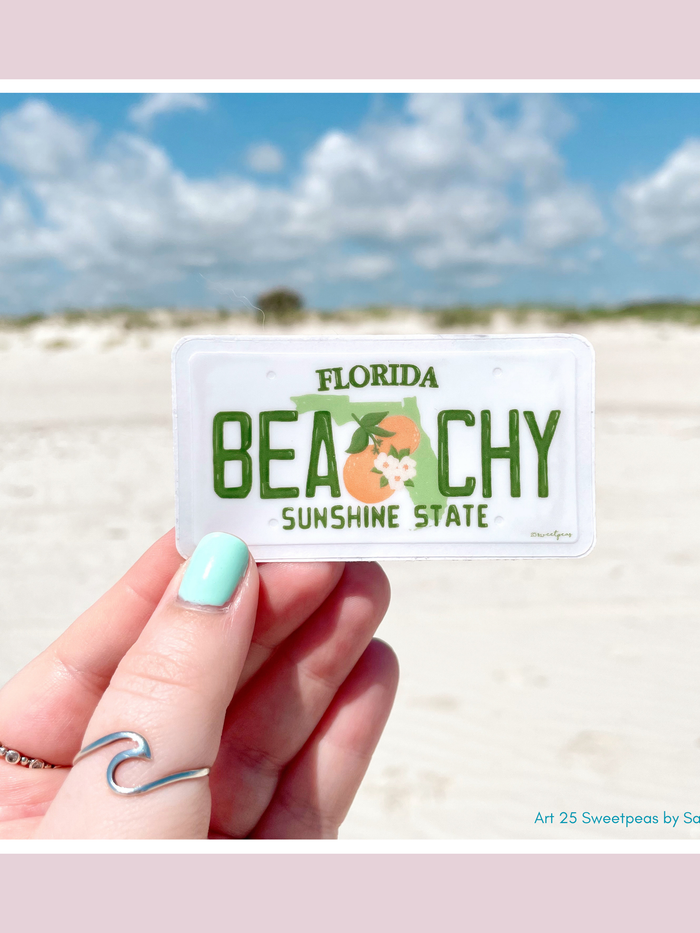 Beachy Florida license plate sticker with orange fruit design held at beach