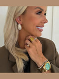 Close-up of woman wearing silver crystal teardrop hoop earrings with gold rings and watch