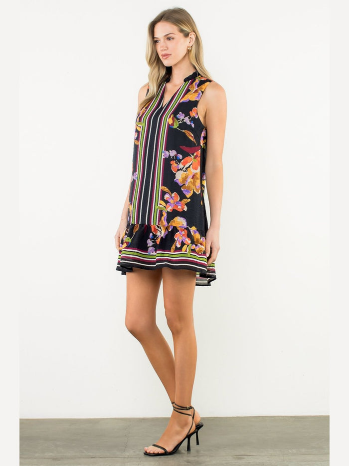 Side angle of black sleeveless floral mini dress with mixed print pattern, striped accents, and ruffled hem detail